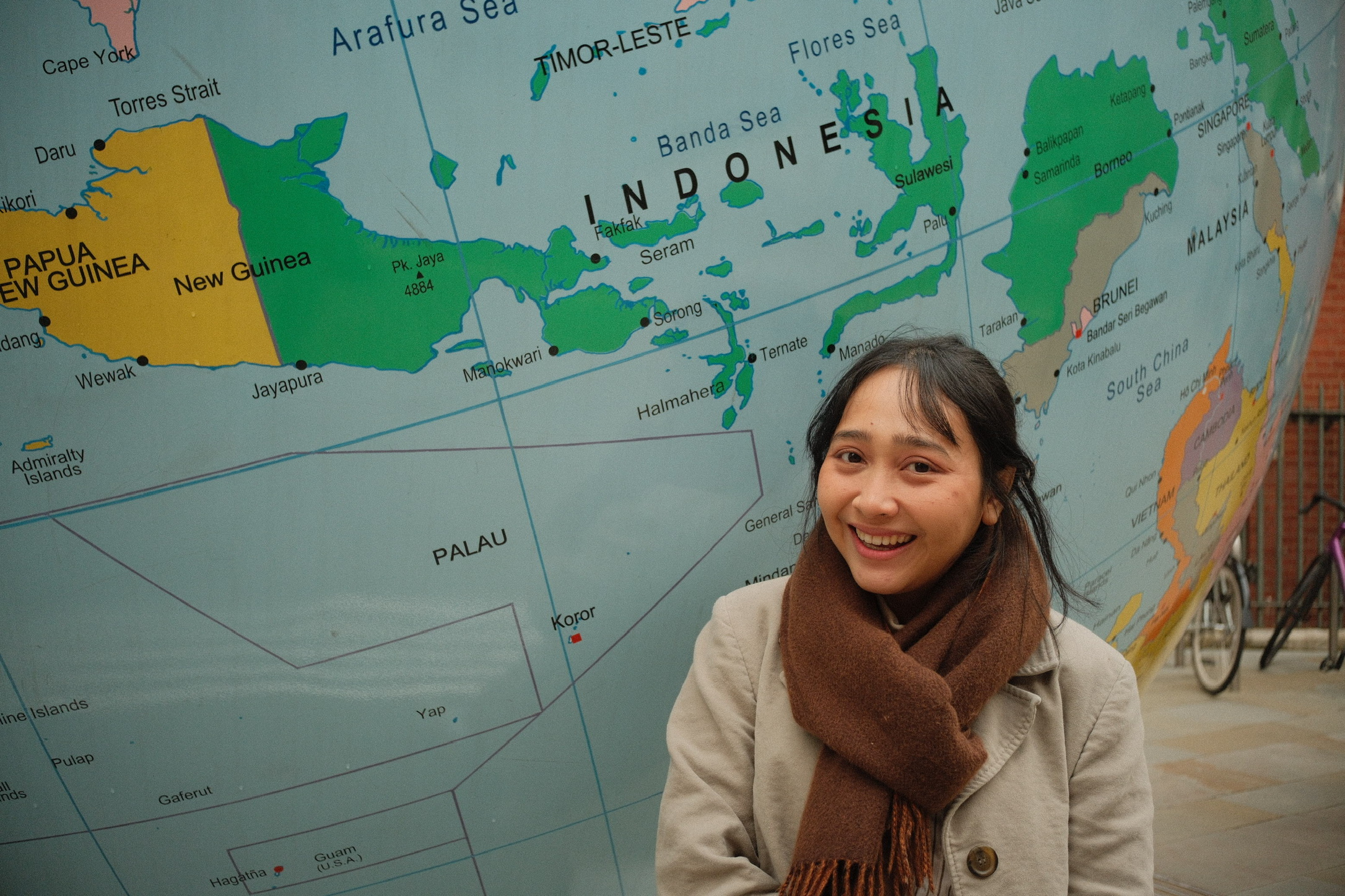 Oktafia in front of a world map, smiling, with Indonesia visible behind her.